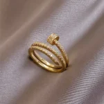 Gold-plated stainless steel adjustable ring with a spiral nail design and embedded clear stones on a satin background.