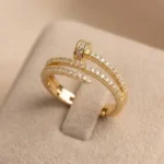 Gold-plated stainless steel adjustable ring with a spiral nail design and embedded clear stones on a satin background.