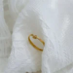 Gold-plated stainless steel minimalist tie knot finger ring held in hand and worn on finger