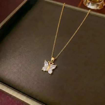 Gold-plated stainless steel butterfly pendant necklace with four clear stones on a dark brown display tray.