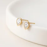 Gold-plated stainless steel teardrop bezel stud earrings with clear stones on a white background
