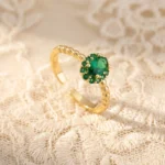 Gold-plated stainless steel open ring with a central oval green stone surrounded by smaller green gems and a twisted rope band.