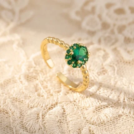 Gold-plated stainless steel open ring with a central oval green stone surrounded by smaller green gems and a twisted rope band.