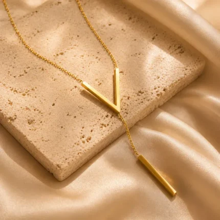 Gold-plated stainless steel Vertex V Lariat Necklace with geometric bar pendant on beige stone background
