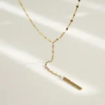 Gold-plated stainless steel lariat necklace with a vertical bar pendant on a white background