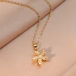 Gold-plated stainless steel necklace featuring a swirling five-petal flower pendant with clear faceted stones on a pink satin background.
