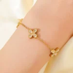 Gold-plated stainless steel chain bracelet featuring three four-petal clover charms with clear stones on a wrist.