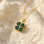 Gold-plated stainless steel four-leaf clover pendant necklace with emerald green heart-shaped stones on lace background