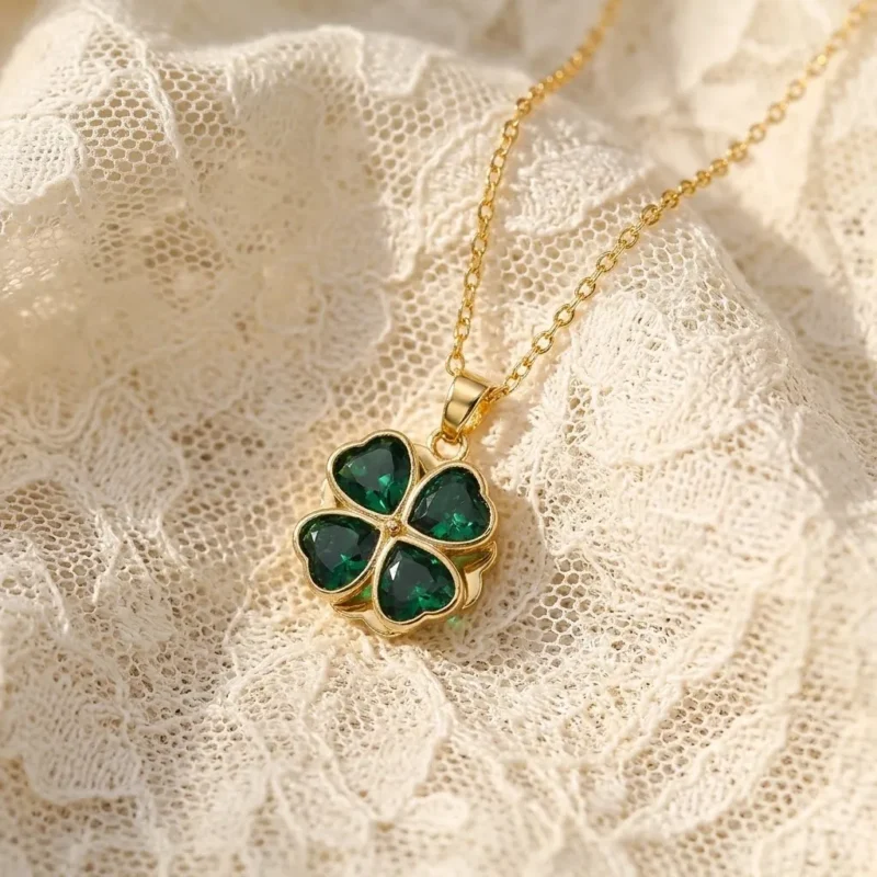Gold-plated stainless steel four-leaf clover pendant necklace with emerald green heart-shaped stones on lace background