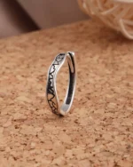 Silver-tone stainless steel ring with black oxidized crackle texture pattern on a cork surface