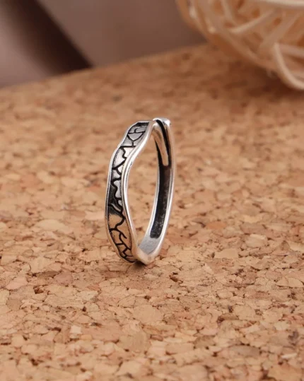 Silver-tone stainless steel ring with black oxidized crackle texture pattern on a cork surface