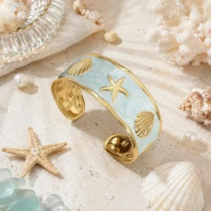 Gold-plated cuff bracelet with light blue enamel, starfish, and shell motifs on sand