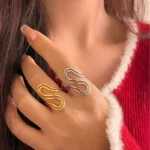 Gold and silver stainless steel S-curve statement rings worn on a hand and displayed on a beach log.