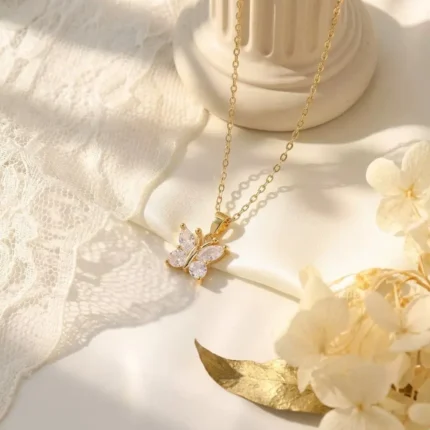 Gold-plated stainless steel butterfly pendant necklace with four clear stones on a dark brown display tray.