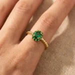 Gold-plated stainless steel open ring with a central oval green stone surrounded by smaller green gems and a twisted rope band.