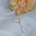 Gold-plated stainless steel Vertex V Lariat Necklace with geometric bar pendant on beige stone background