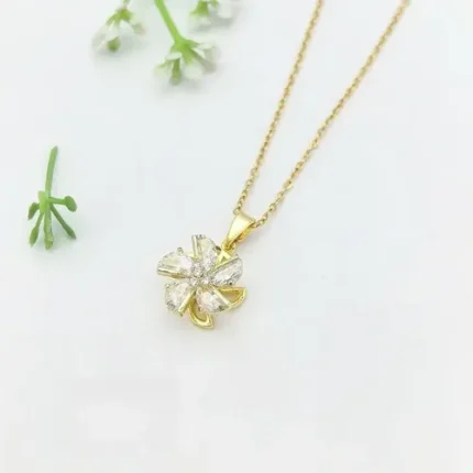 Gold-plated stainless steel necklace featuring a swirling five-petal flower pendant with clear faceted stones on a pink satin background.