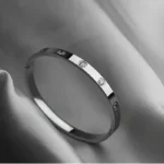 Silver stainless steel bangle bracelet with round clear stone accents on a dark textured background