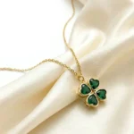 Gold-plated stainless steel four-leaf clover pendant necklace with emerald green heart-shaped stones on lace background