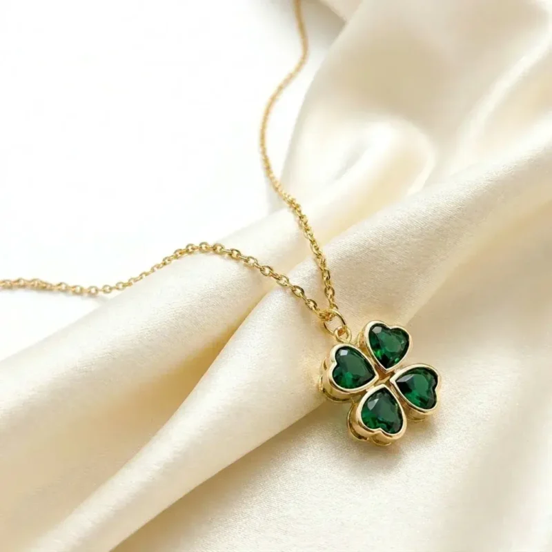 Gold-plated stainless steel four-leaf clover pendant necklace with emerald green heart-shaped stones on lace background