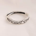 Silver-tone stainless steel ring with black oxidized crackle texture pattern on a cork surface