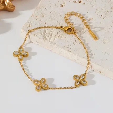 Gold-plated stainless steel chain bracelet featuring three four-petal clover charms with clear stones on a wrist.