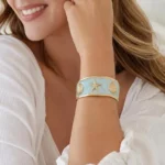 Gold-plated cuff bracelet with light blue enamel, starfish, and shell motifs on sand