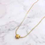 Gold plated stainless steel star pendant necklace on a delicate chain displayed on textured backgrounds