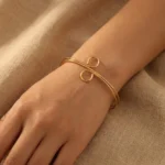 Gold-plated stainless steel spiral loop cuff bracelet on beige fabric background