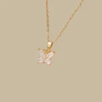 Gold-plated stainless steel butterfly pendant necklace with four clear stones on a dark brown display tray.