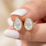 Gold-plated stainless steel teardrop bezel stud earrings with clear stones on a white background