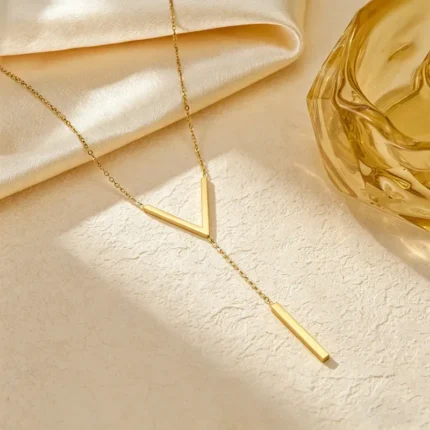 Gold-plated stainless steel Vertex V Lariat Necklace with geometric bar pendant on beige stone background