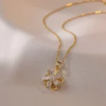 Gold-plated stainless steel necklace featuring a swirling five-petal flower pendant with clear faceted stones on a pink satin background.