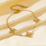 Gold-plated stainless steel chain bracelet featuring three four-petal clover charms with clear stones on a wrist.