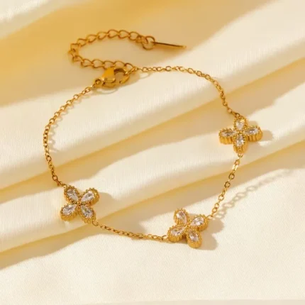 Gold-plated stainless steel chain bracelet featuring three four-petal clover charms with clear stones on a wrist.