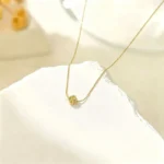 Gold-plated stainless steel necklace with a small four-leaf clover pendant on a textured stone surface.