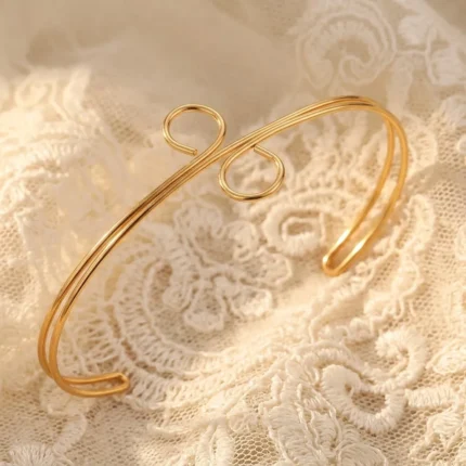 Gold-plated stainless steel spiral loop cuff bracelet on beige fabric background