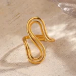 Gold and silver stainless steel S-curve statement rings worn on a hand and displayed on a beach log.