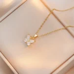 Gold-plated stainless steel butterfly pendant necklace with four clear stones on a dark brown display tray.