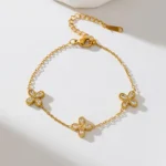 Gold-plated stainless steel chain bracelet featuring three four-petal clover charms with clear stones on a wrist.