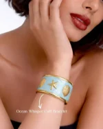 Gold-plated cuff bracelet with light blue enamel, starfish, and shell motifs on sand