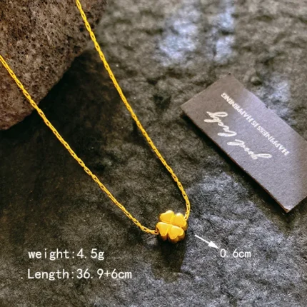 Gold-plated stainless steel necklace with a small four-leaf clover pendant on a textured stone surface.