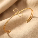 Gold-plated stainless steel spiral loop cuff bracelet on beige fabric background
