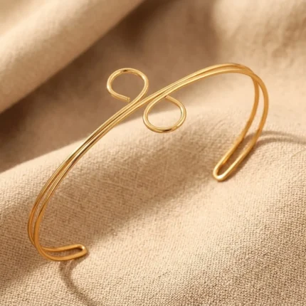 Gold-plated stainless steel spiral loop cuff bracelet on beige fabric background