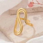 Gold and silver stainless steel S-curve statement rings worn on a hand and displayed on a beach log.