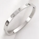 Silver stainless steel bangle bracelet with round clear stone accents on a dark textured background