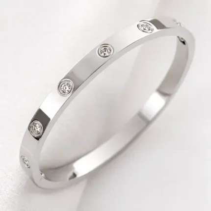 Silver stainless steel bangle bracelet with round clear stone accents on a dark textured background